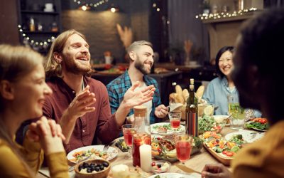 Group of emotional young people enjoying dinner party with friends and smiling happily sitting at table in dimly lit room, copy space